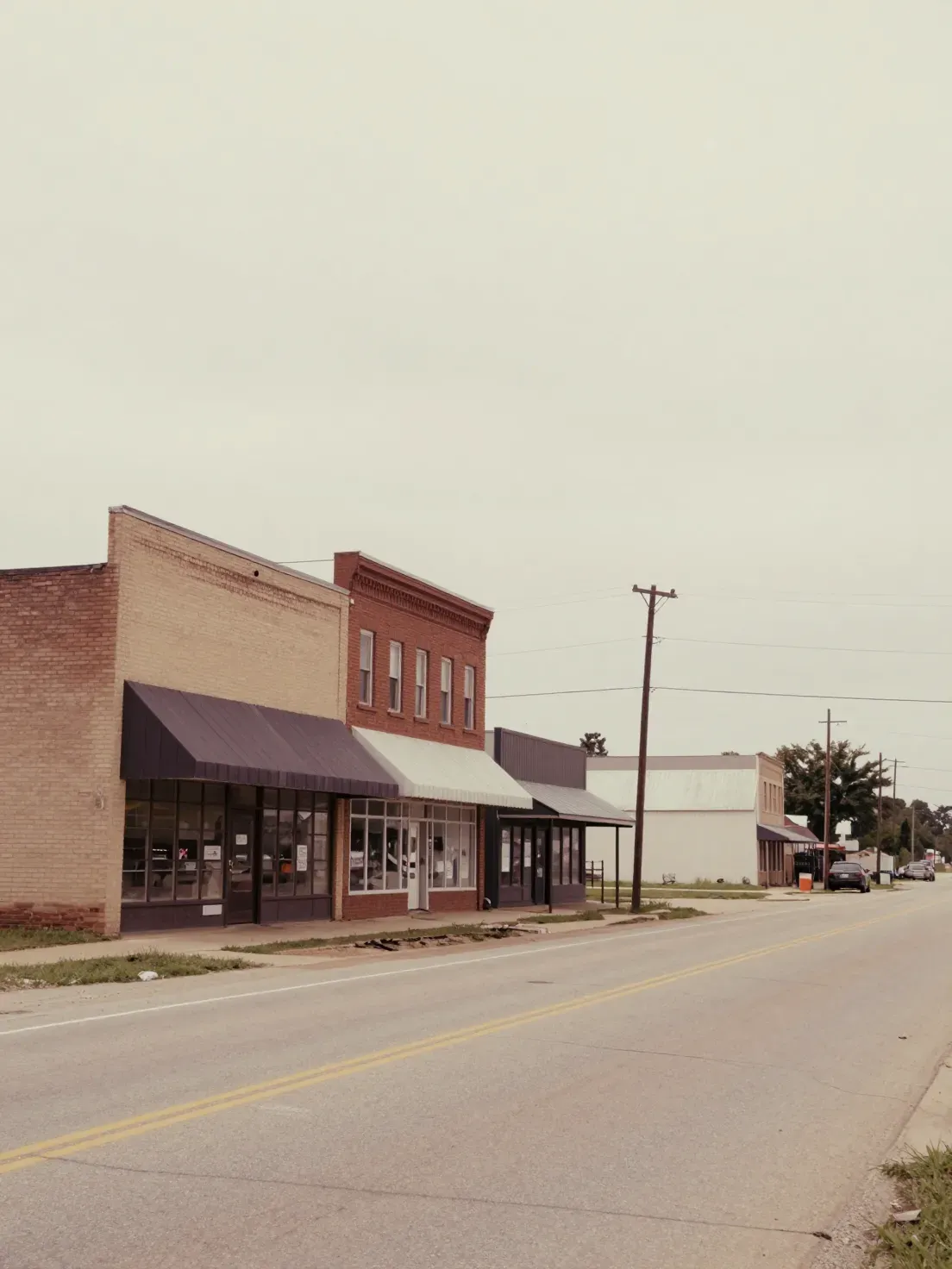 A main street of low brick storefronts in a small Kansas town under an overcast sky